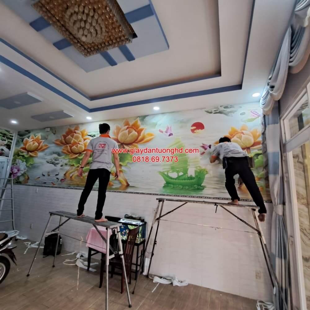 Đội ngũ thợ chuyên nghiệp đang hoàn thiện bức tranh dán tường 3D phong cảnh hoa sen vàng và thuyền buồm tài lộc, mang lại vượng khí cho phòng khách tại Quận 2