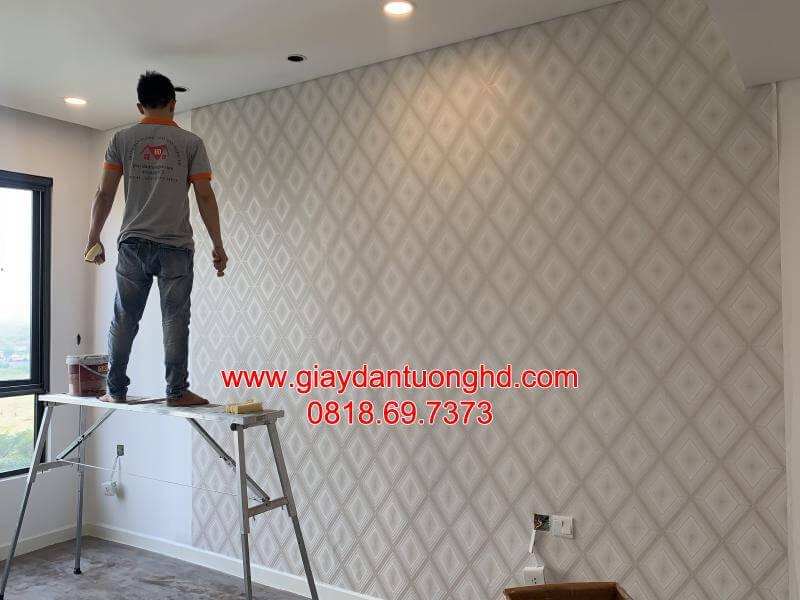 Thợ thi công đang dán mẫu giấy dán tường họa tiết hình thoi 3D màu xám nhạt đan xen tinh tế trên mảng tường lớn phòng ngủ