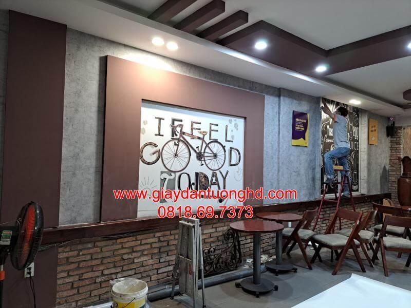 Thợ đang đứng trên thang thi công dán tranh tường 3D họa tiết chữ và xe đạp hiện đại kết hợp nền giả bê tông cho quán cà phê.